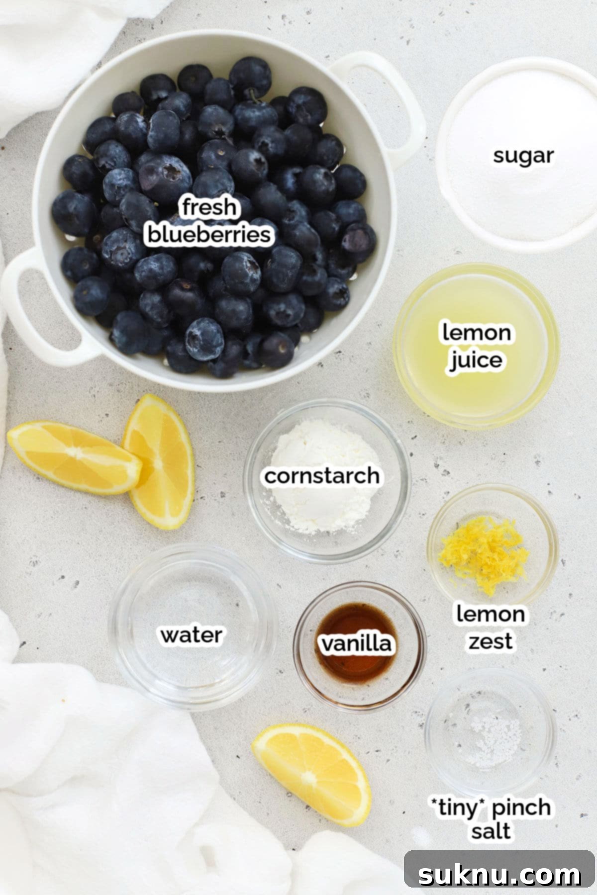 Easy Blueberry Sauce For Cheesecake And Beyond 3 A flat lay photograph showcasing all the fresh, simple ingredients required to prepare homemade blueberry sauce: fresh blueberries, granulated sugar, fresh lemon, cornstarch, and vanilla extract.