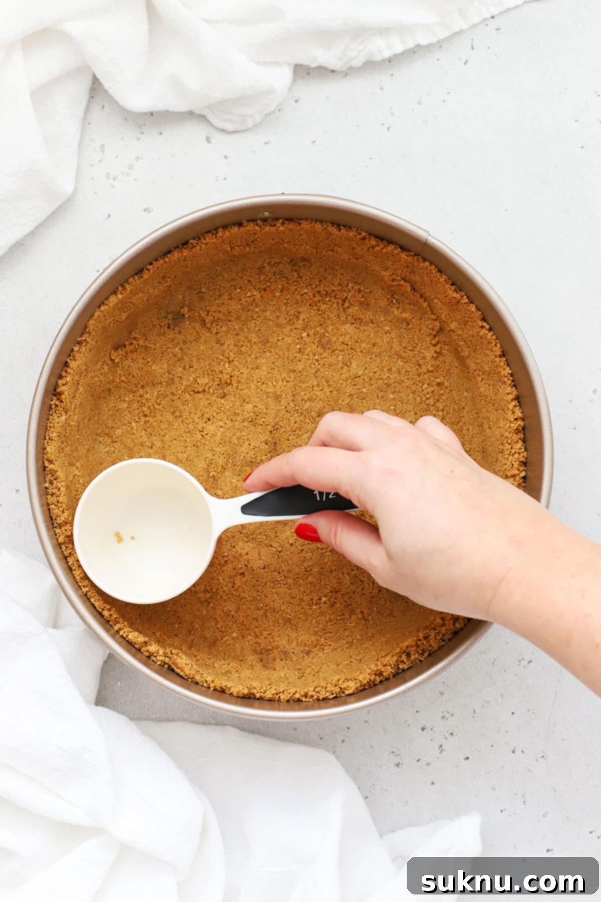 Luscious Gluten-Free Blueberry Cheesecake 4 Hands pressing gluten-free graham cracker crumbs into a springform pan to form the cheesecake crust.
