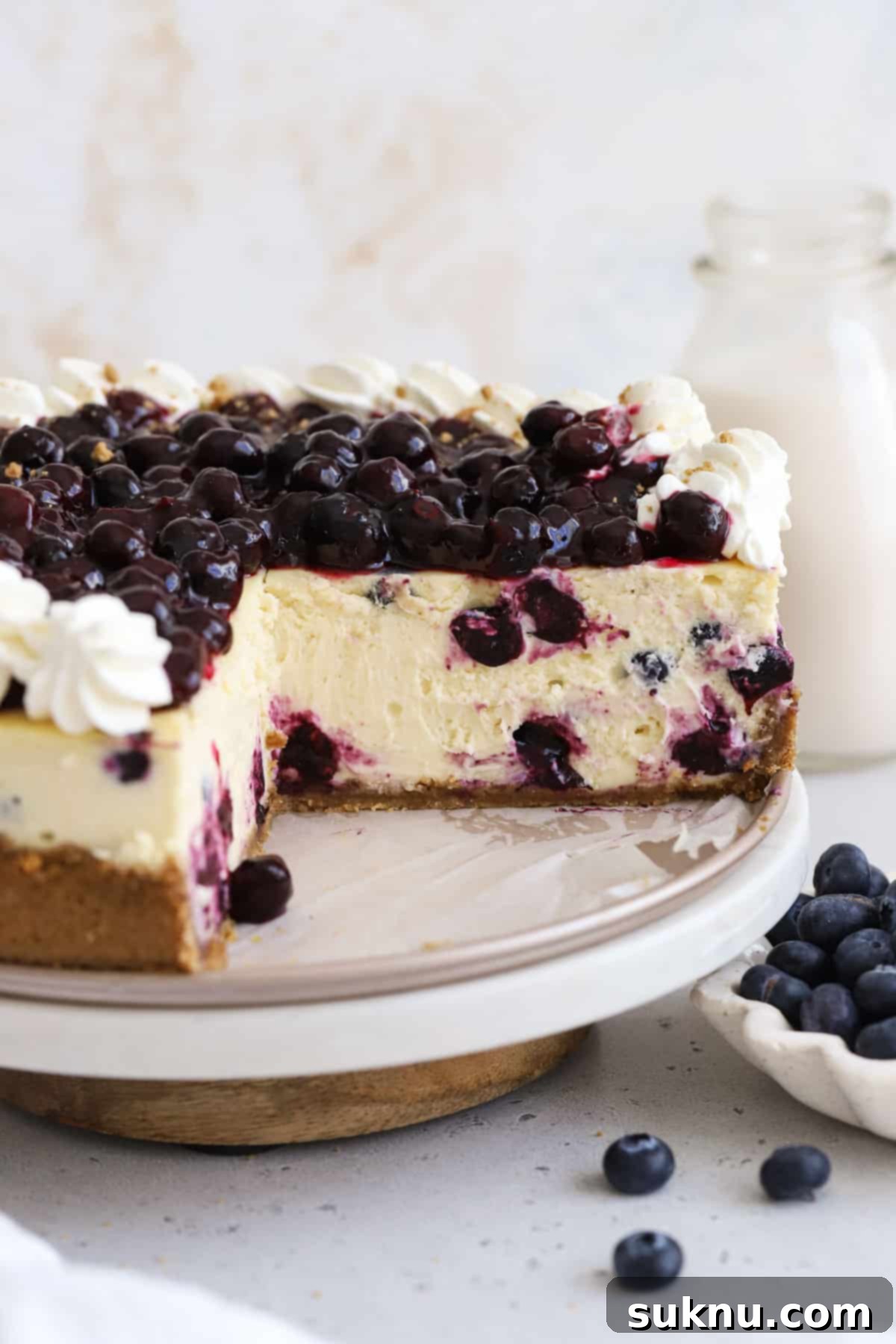 Luscious Gluten-Free Blueberry Cheesecake 7 A stunning gluten-free blueberry cheesecake adorned with elegant swirls of whipped cream and a generous layer of fresh blueberry topping, ready for serving.