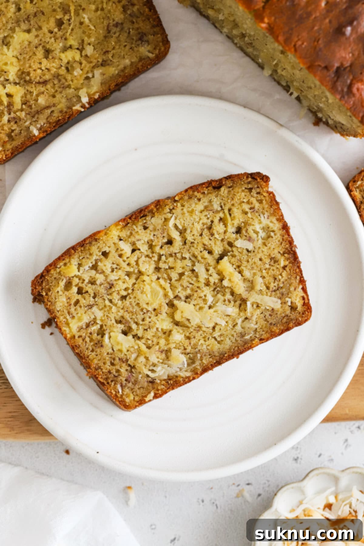 A perfectly sliced piece of gluten-free pineapple coconut banana bread on a white dessert plate, showcasing its moist texture and tropical ingredients.