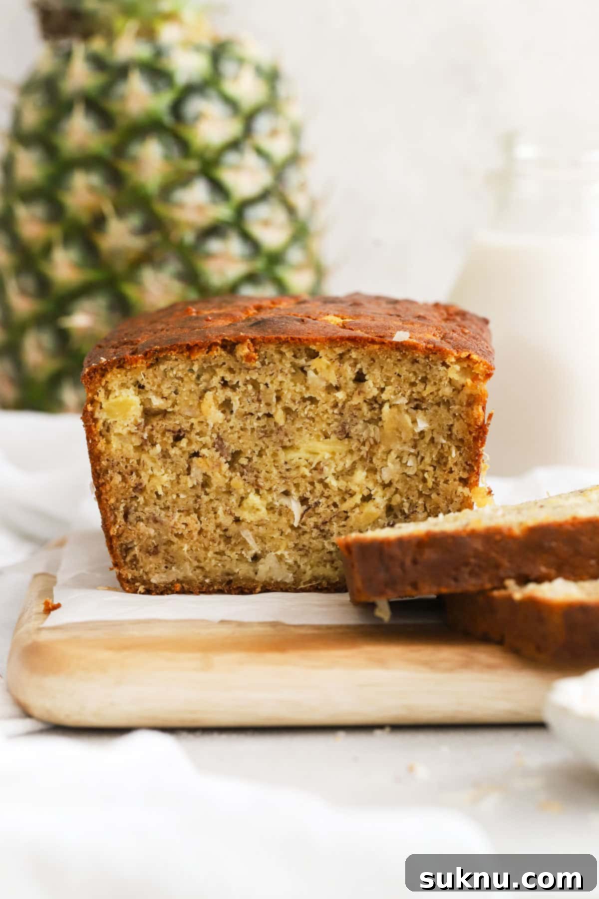 A freshly baked loaf of gluten-free banana bread with visible pineapple and coconut pieces, presented beautifully on a wire cooling rack.