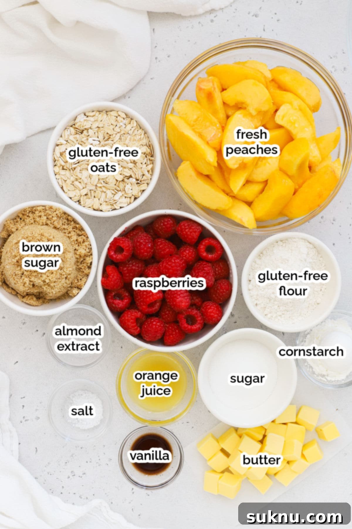 A collection of fresh ingredients including peaches, raspberries, oats, and flour, arranged for making gluten-free raspberry peach crisp.