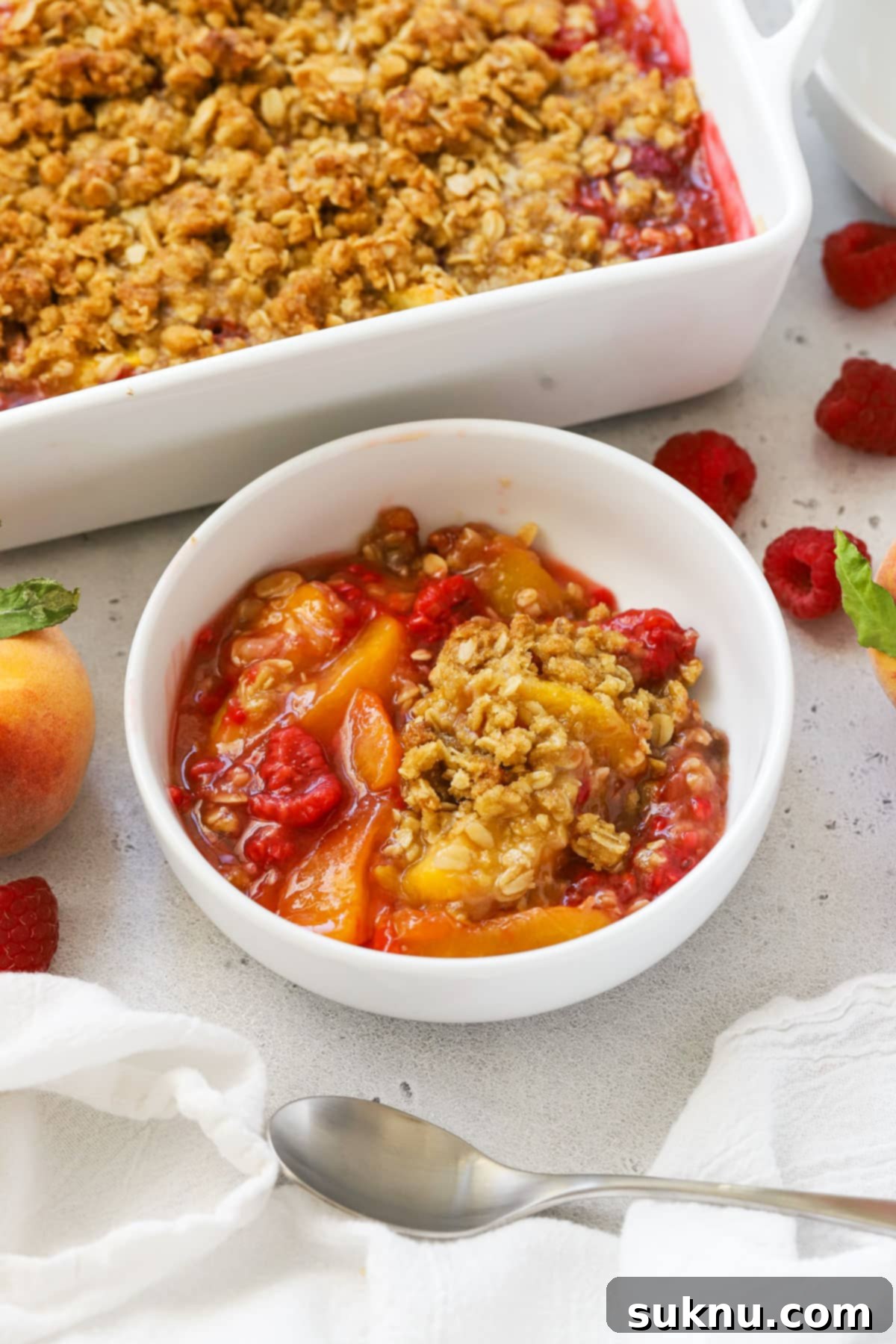 A delightful bowl of raspberry peach crisp with its golden, crunchy oat crumble topping visible, ready to be enjoyed.