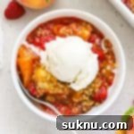 A bowl of raspberry peach crisp topped with a scoop of vanilla ice cream