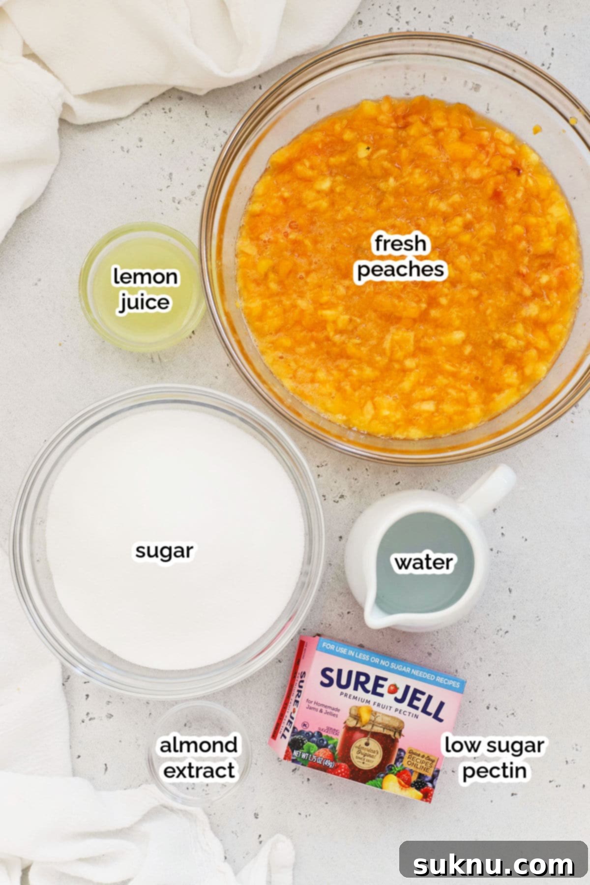 Effortless Low Sugar Peach Freezer Jam 3 Ingredients for peach freezer jam laid out on a table, including fresh peaches, lemon juice, sugar, and pectin.