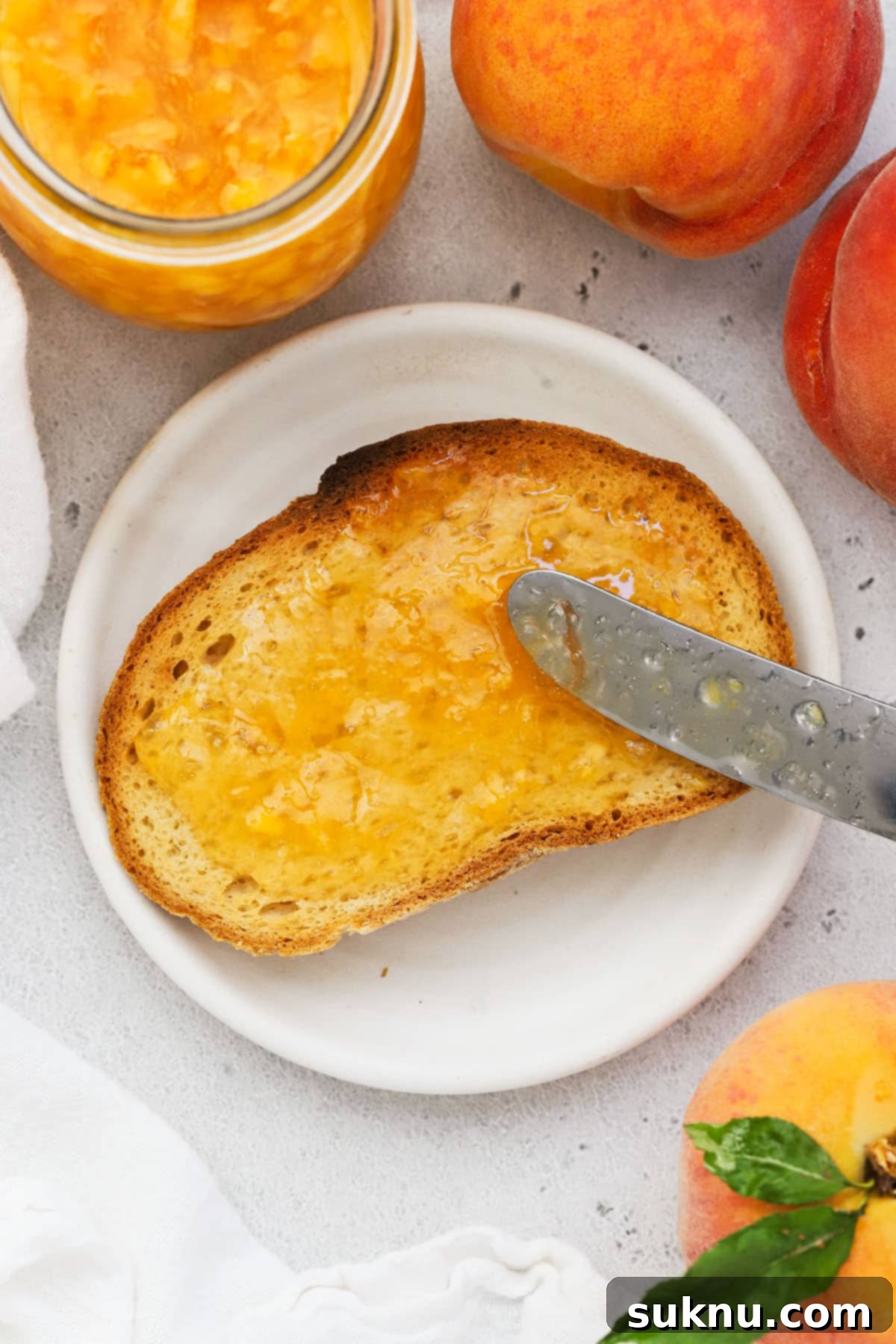 Effortless Low Sugar Peach Freezer Jam 5 Homemade peach freezer jam being spread generously on a slice of gluten-free toast.