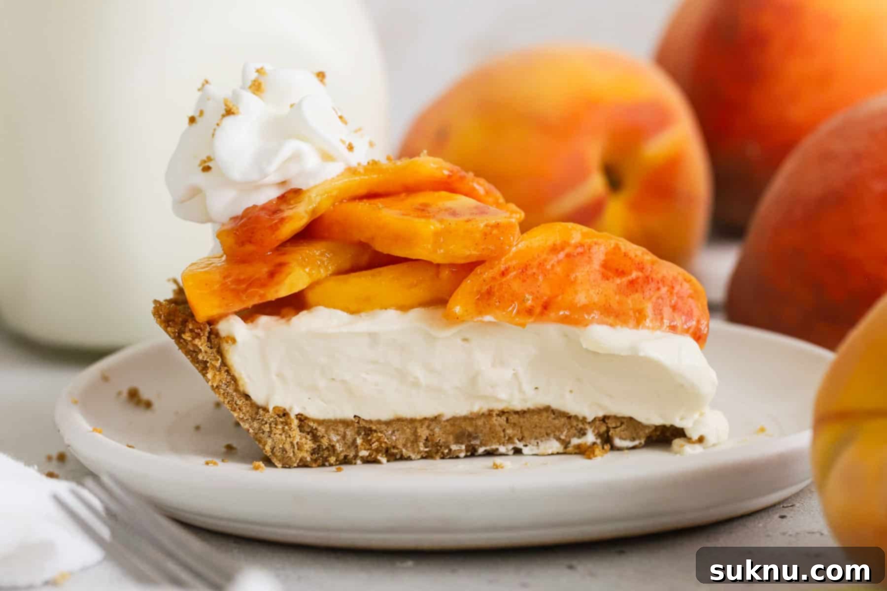 a slice of fresh peach pie with gluten-free graham cracker crust, whipped filling, and fresh peach topping
