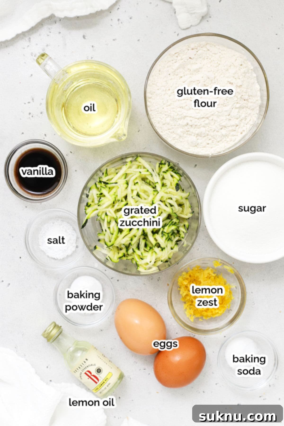 A flat lay image displaying all the ingredients for gluten-free lemon zucchini bread, including fresh lemons, grated zucchini, flour, eggs, and spices.