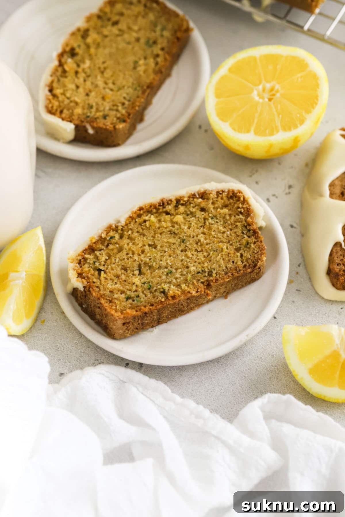 Close-up of perfectly sliced gluten-free lemon zucchini bread on white dessert plates, showing its moist crumb and lemon glaze.