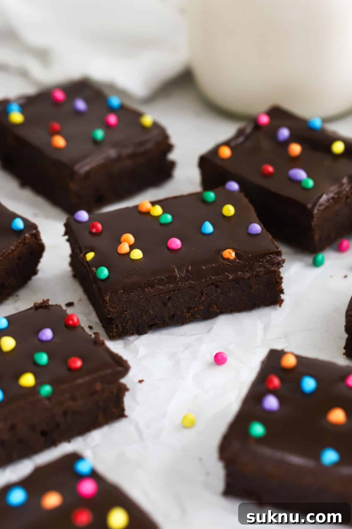 Gluten-free Cosmic brownie squares next to a bottle of milk and a bowl of colorful sprinkles