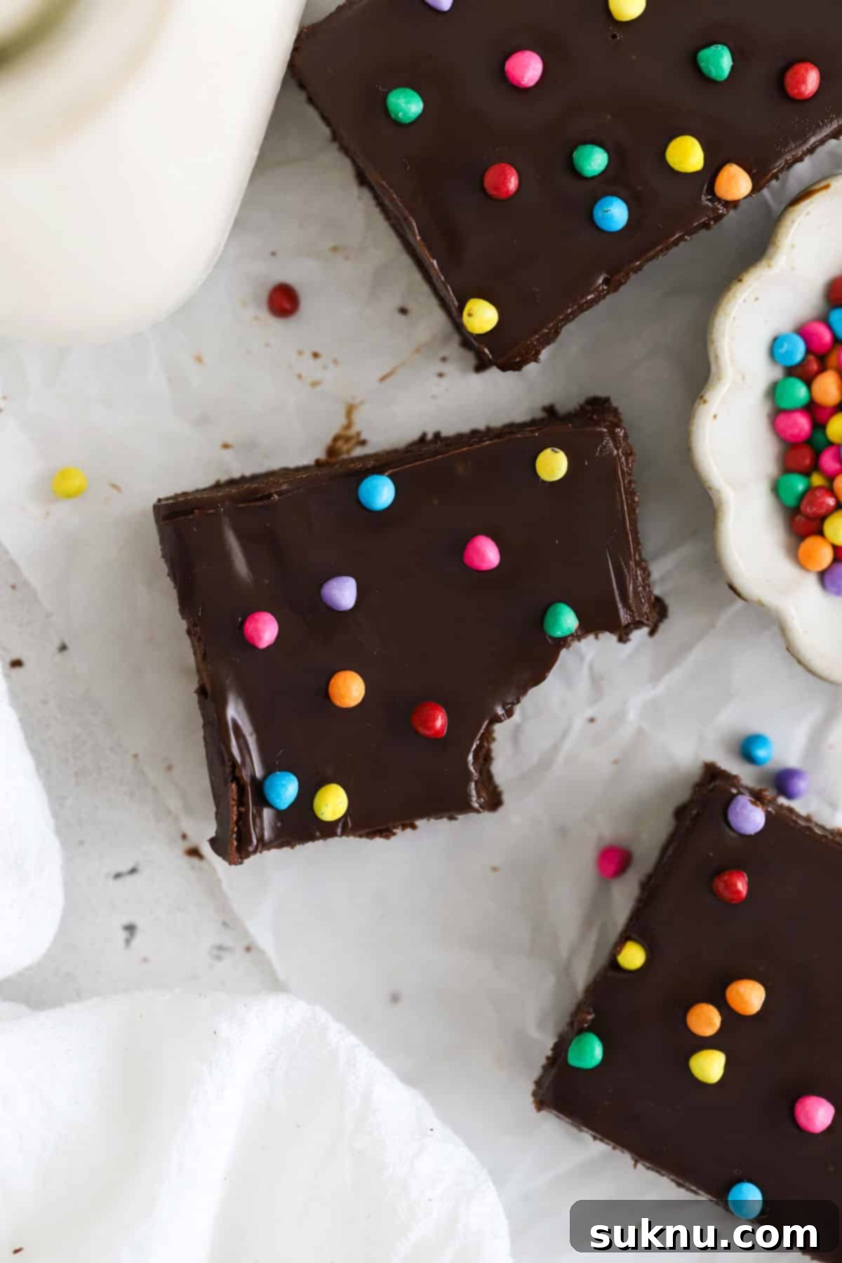 Gluten-free Cosmic brownie squares next to a bottle of milk and a bowl of colorful sprinkles