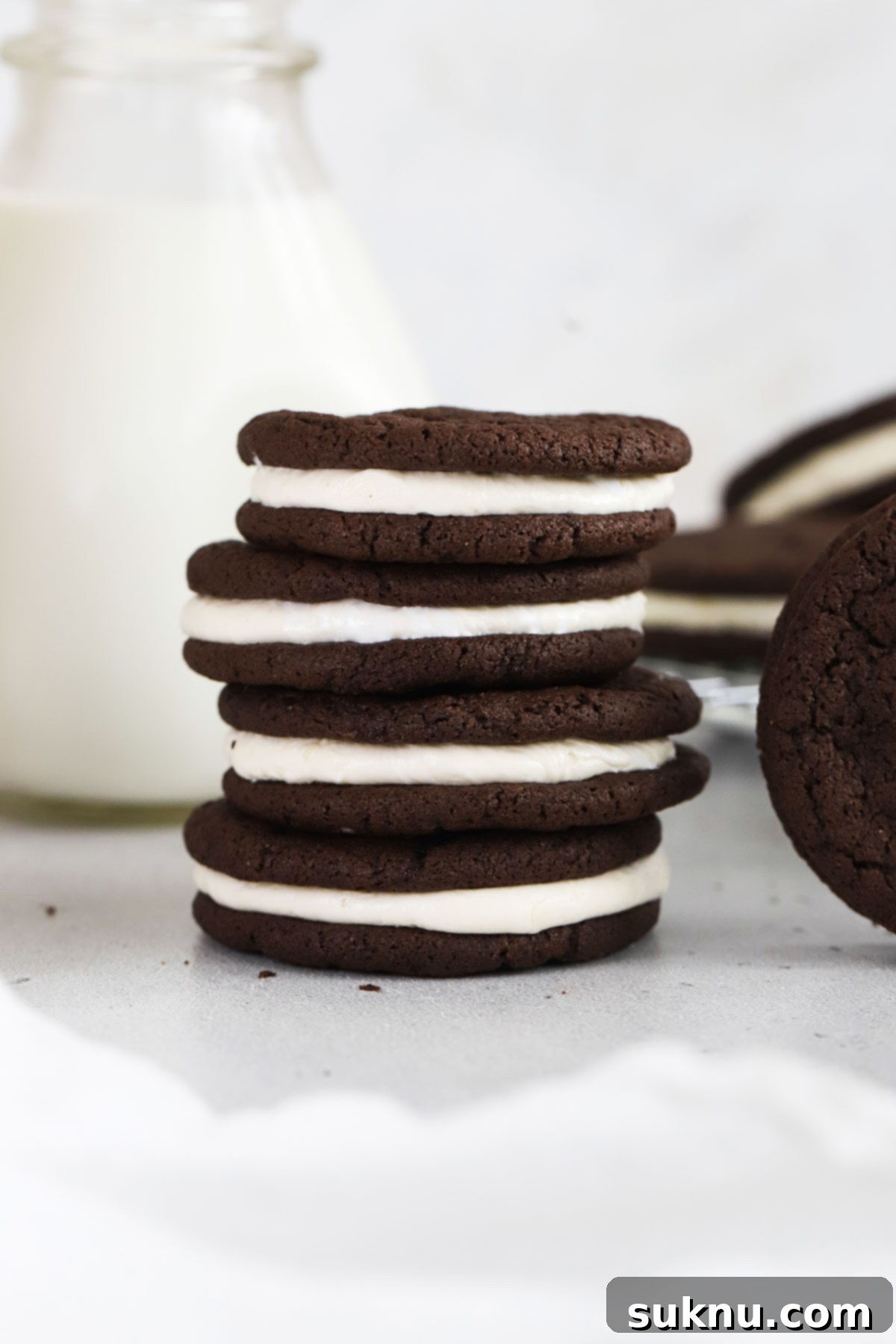 Homemade gluten-free Oreo cookies stacked next to a bottle of milk, showcasing the rich chocolate and creamy vanilla