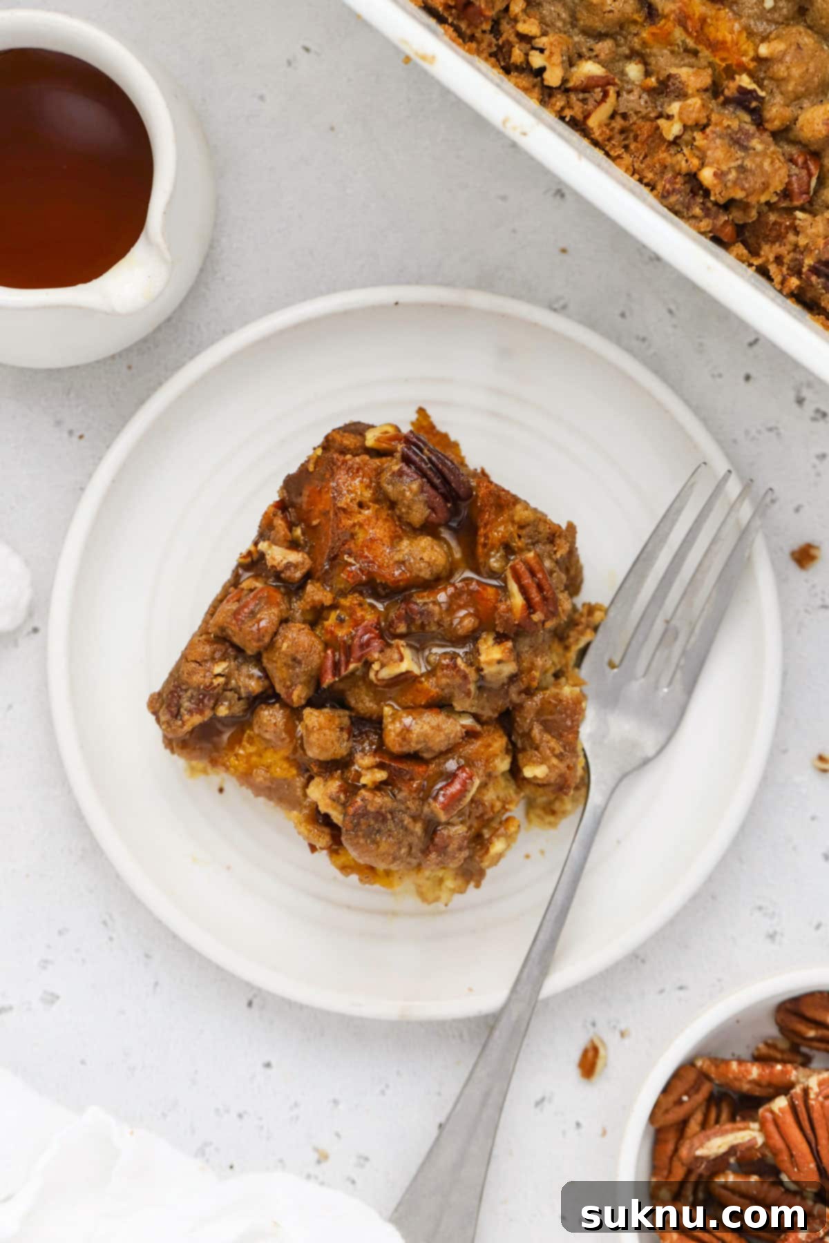 Gluten-Free Pumpkin Spice French Toast Casserole 7 A slice of golden-brown gluten-free pumpkin French toast casserole on a plate, garnished with maple syrup and powdered sugar.