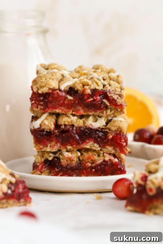 A stack of golden-brown gluten-free cranberry crumble bars on a white plate, revealing the fruity filling and crumbly topping.