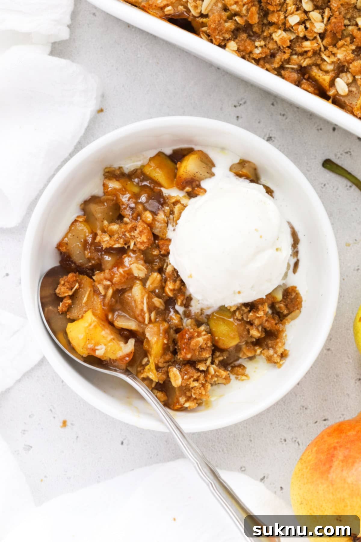 A beautifully presented bowl of gluten-free spiced pear crisp, generously topped with creamy vanilla ice cream and a rich caramel sauce, ready to be enjoyed.