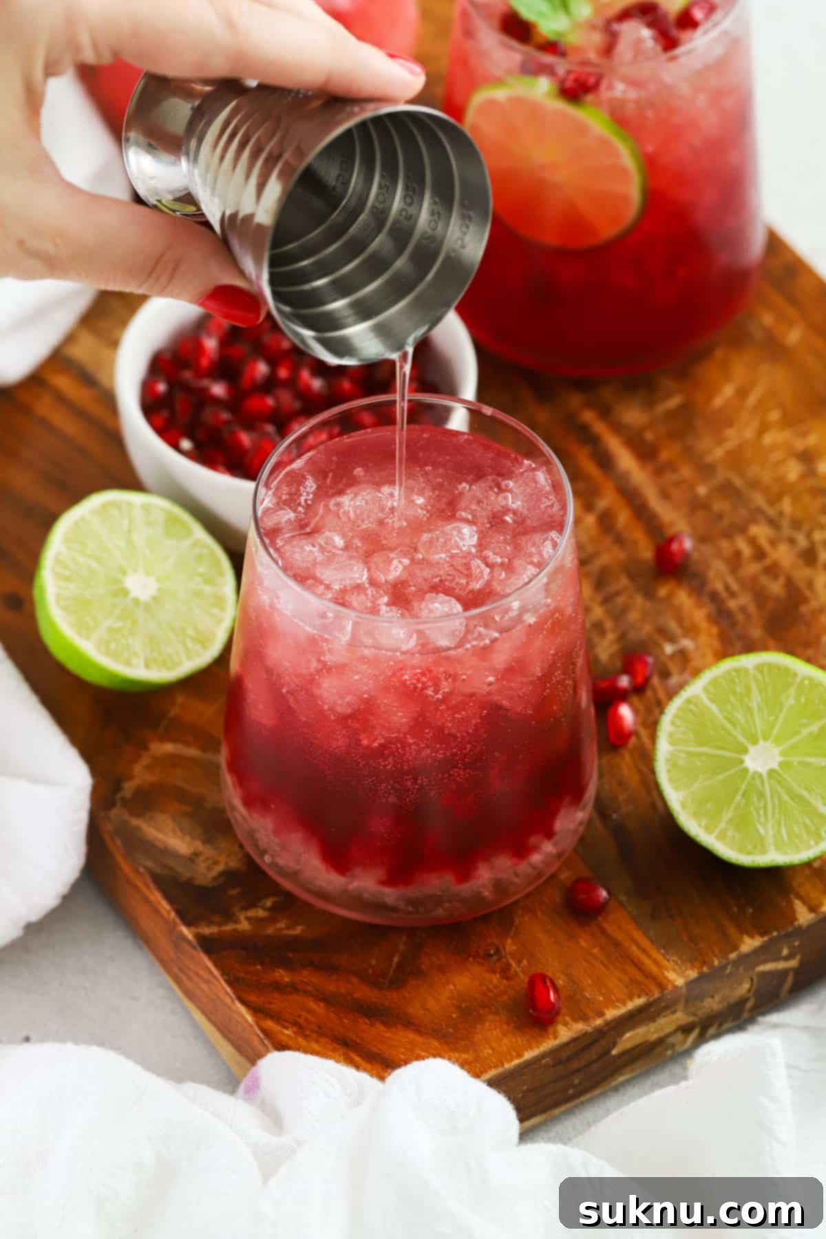 A stream of effervescent ginger beer being poured into a glass filled with a ruby-red pomegranate mixture and ice, creating a visually appealing, refreshing mocktail.