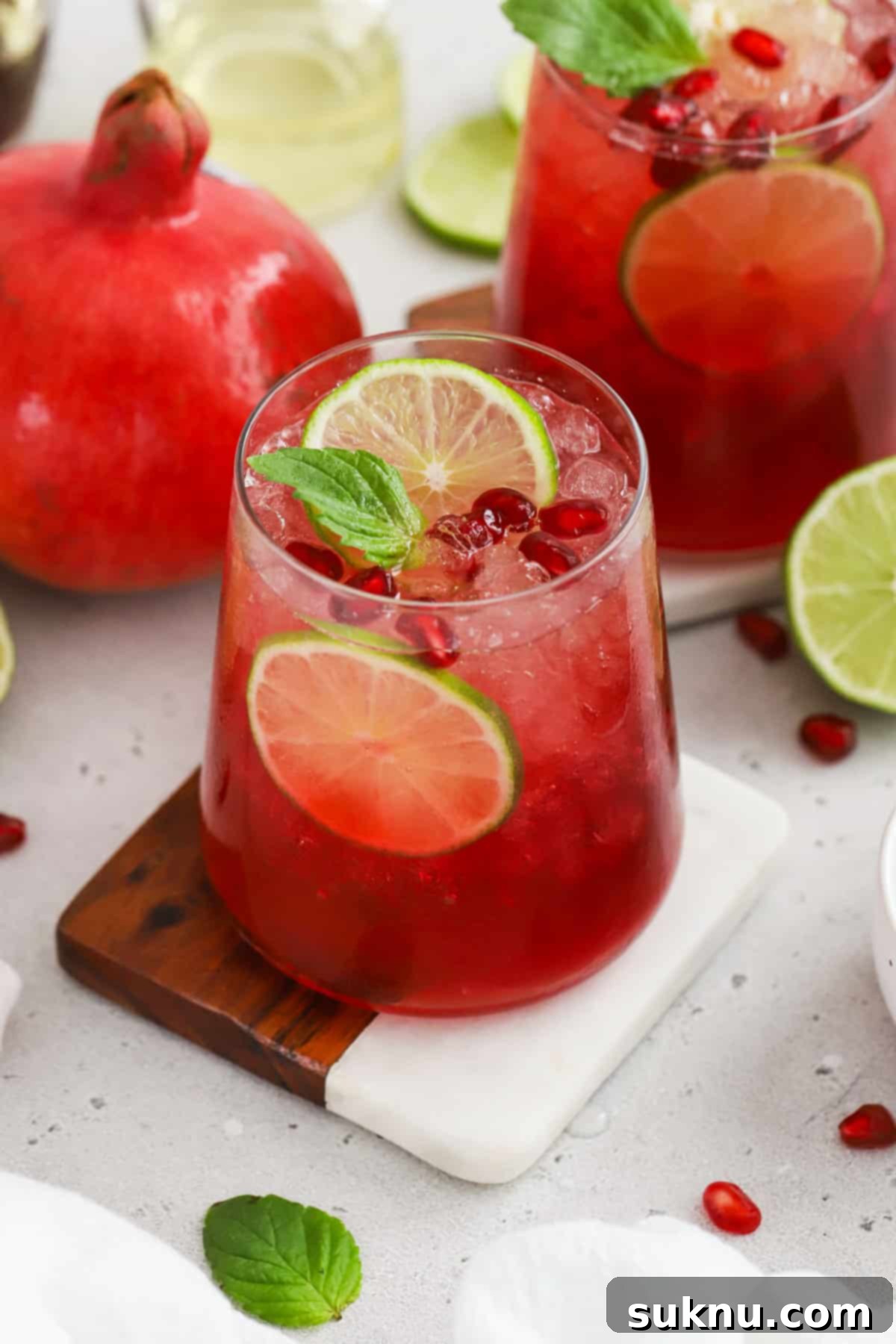 Two ginger pomegranate mocktails, brightly adorned with juicy pomegranate arils, fresh mint sprigs, and lime wheels, ready to be enjoyed at a festive gathering.