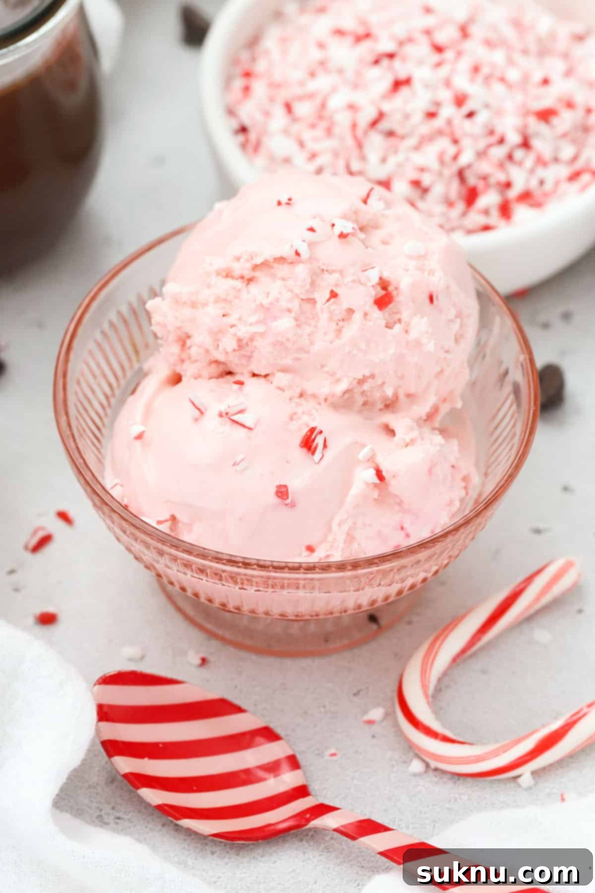 Scoops of Pink candy cane ice cream sprinkled with candy cane bits in a pink dessert bowl