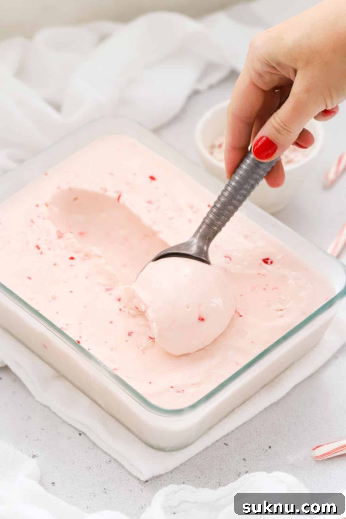 Scooping pink peppermint ice cream from a container
