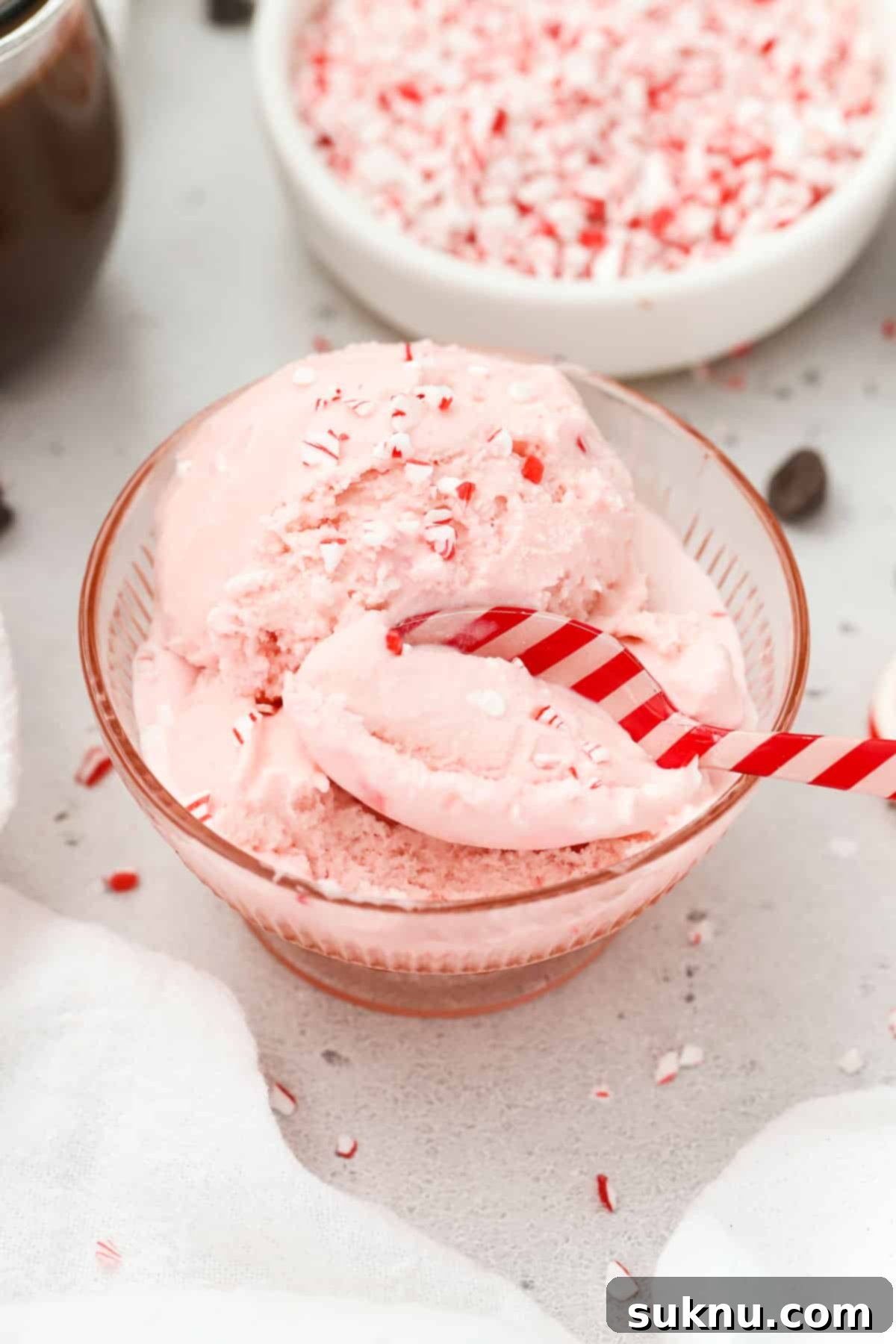 A red and pink striped spoon dipping into a bowl of pink peppermint ice cream with candy cane bits