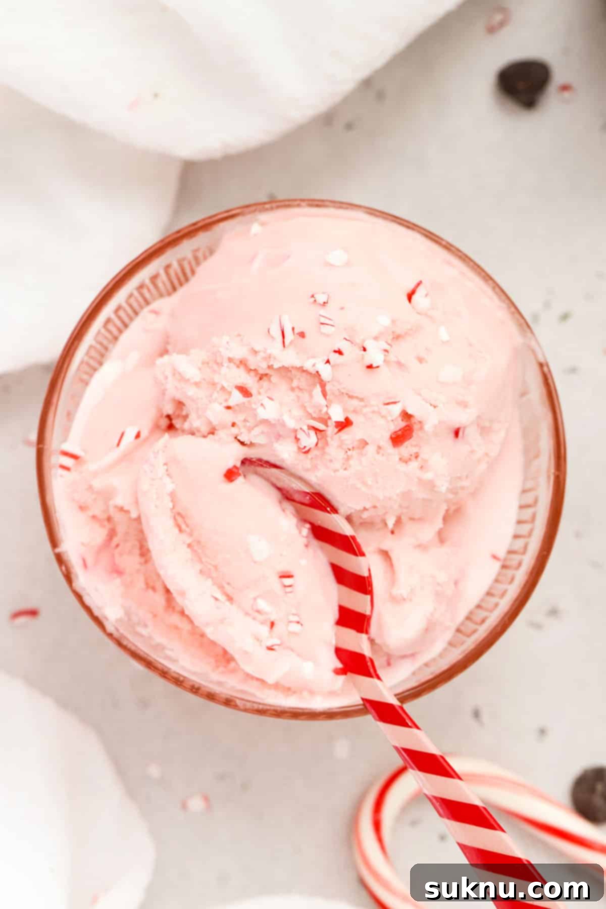 A red and pink striped spoon dipping into a bowl of pink peppermint ice cream with candy cane bits