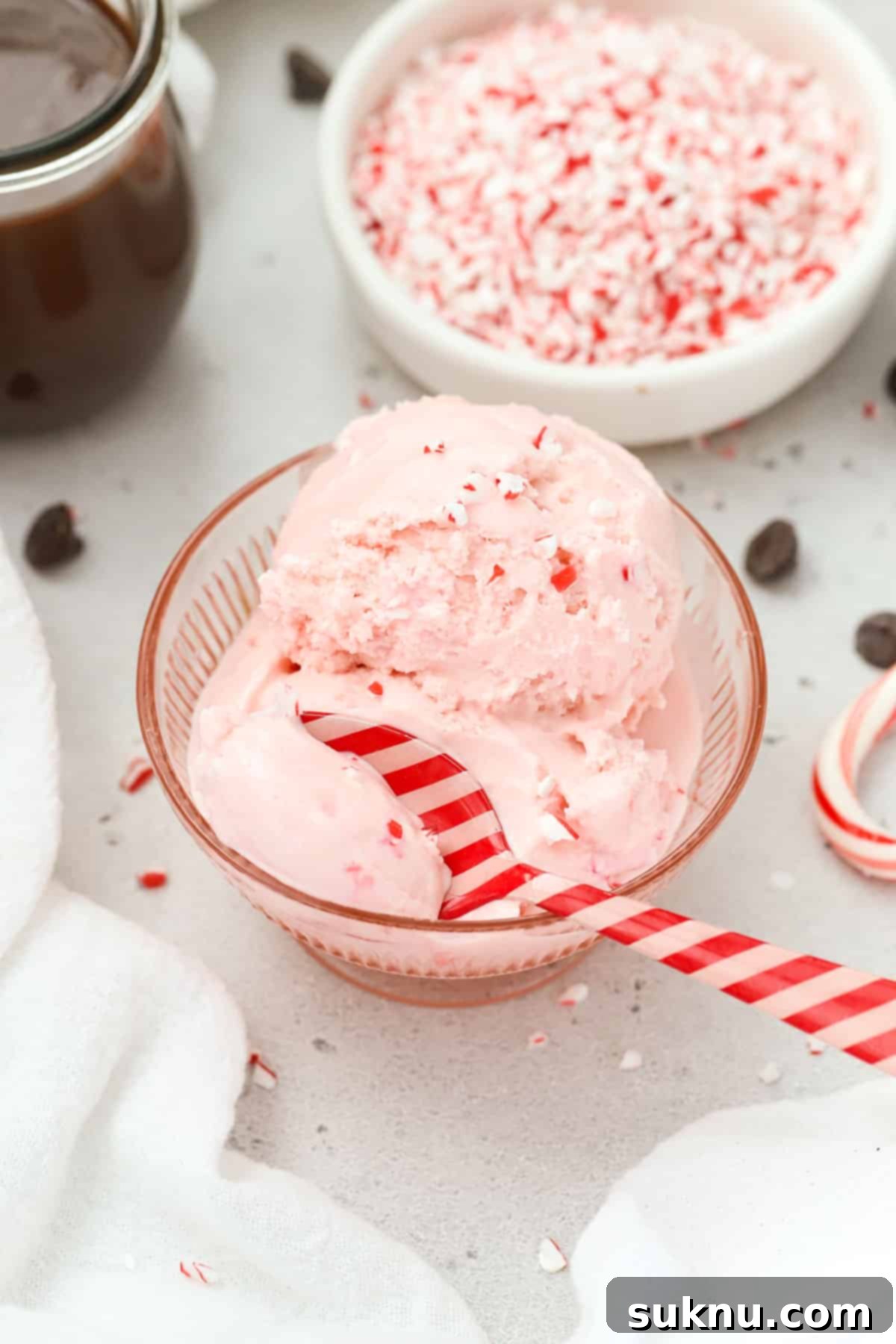 A red and pink striped spoon dipping into a bowl of pink peppermint ice cream with candy cane bits