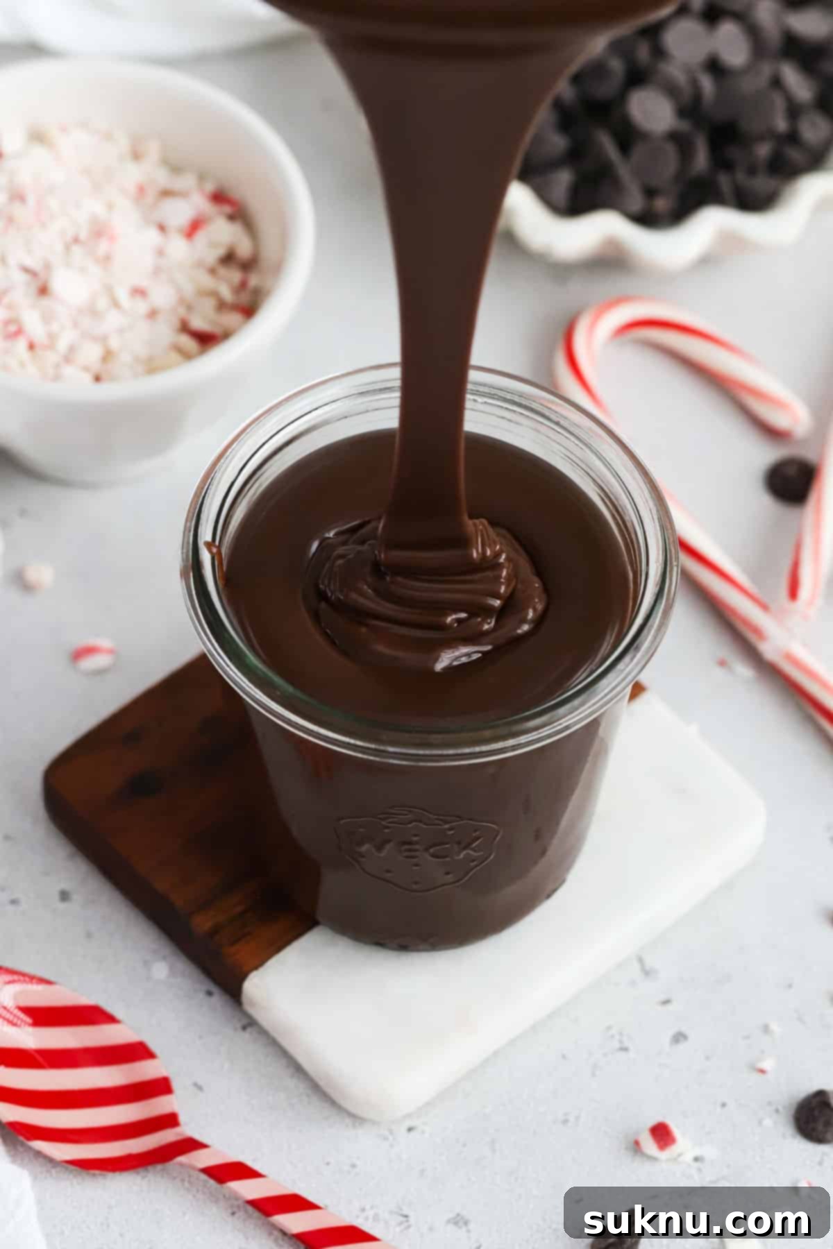 Pouring thick peppermint hot fudge sauce into a glass jar