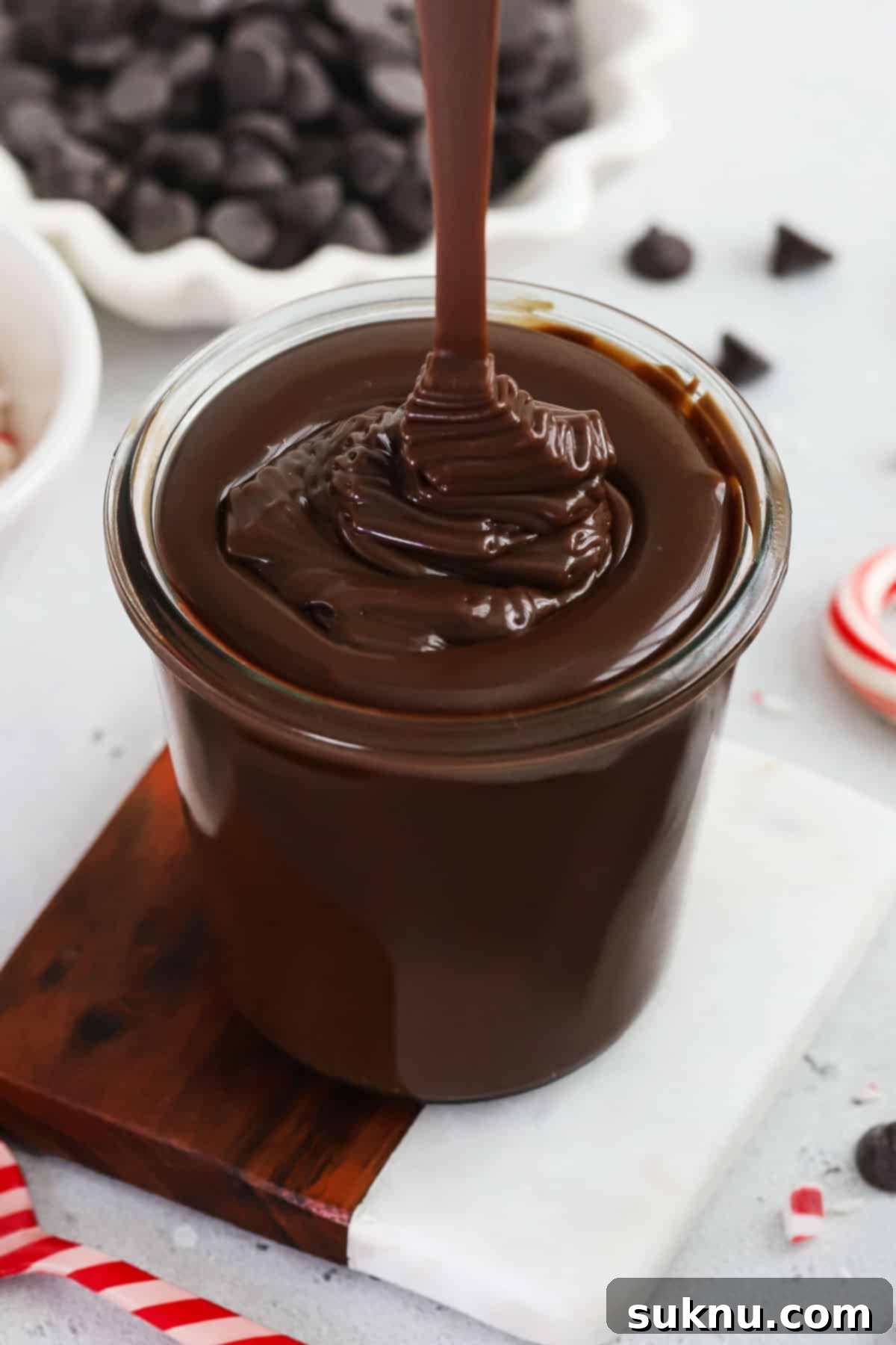 Pouring thick peppermint hot fudge sauce into a glass jar