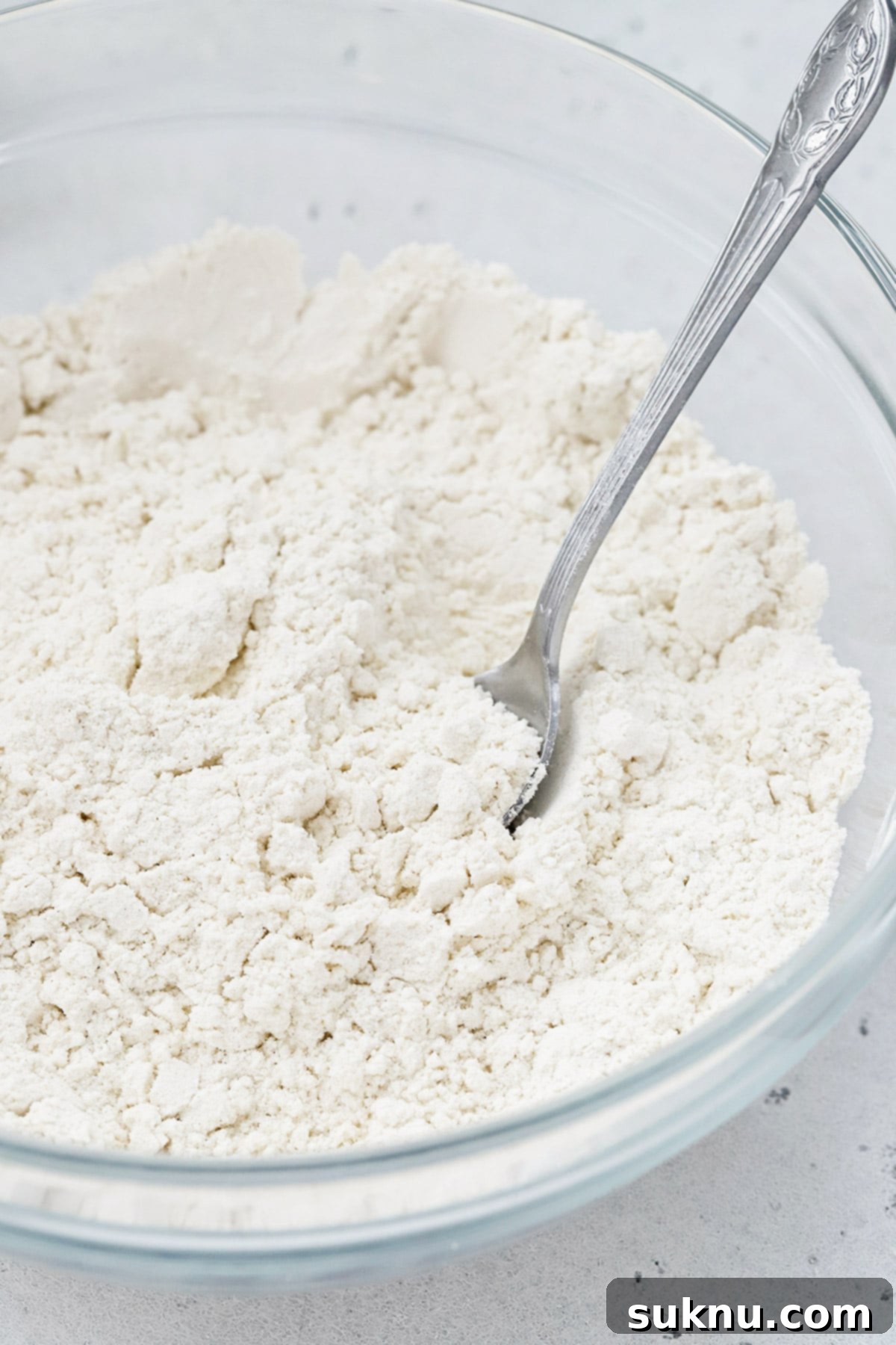 Master Flour Measurement For Perfect Baking 16 Front view of a spoon in a bowl of flour, illustrating the preparation for scooping and leveling