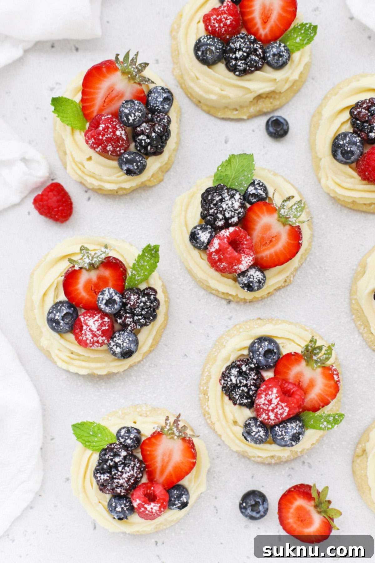 Overhead view of gluten-free fruit pizza cookies topped with cream cheese frosting berries and powdered sugar