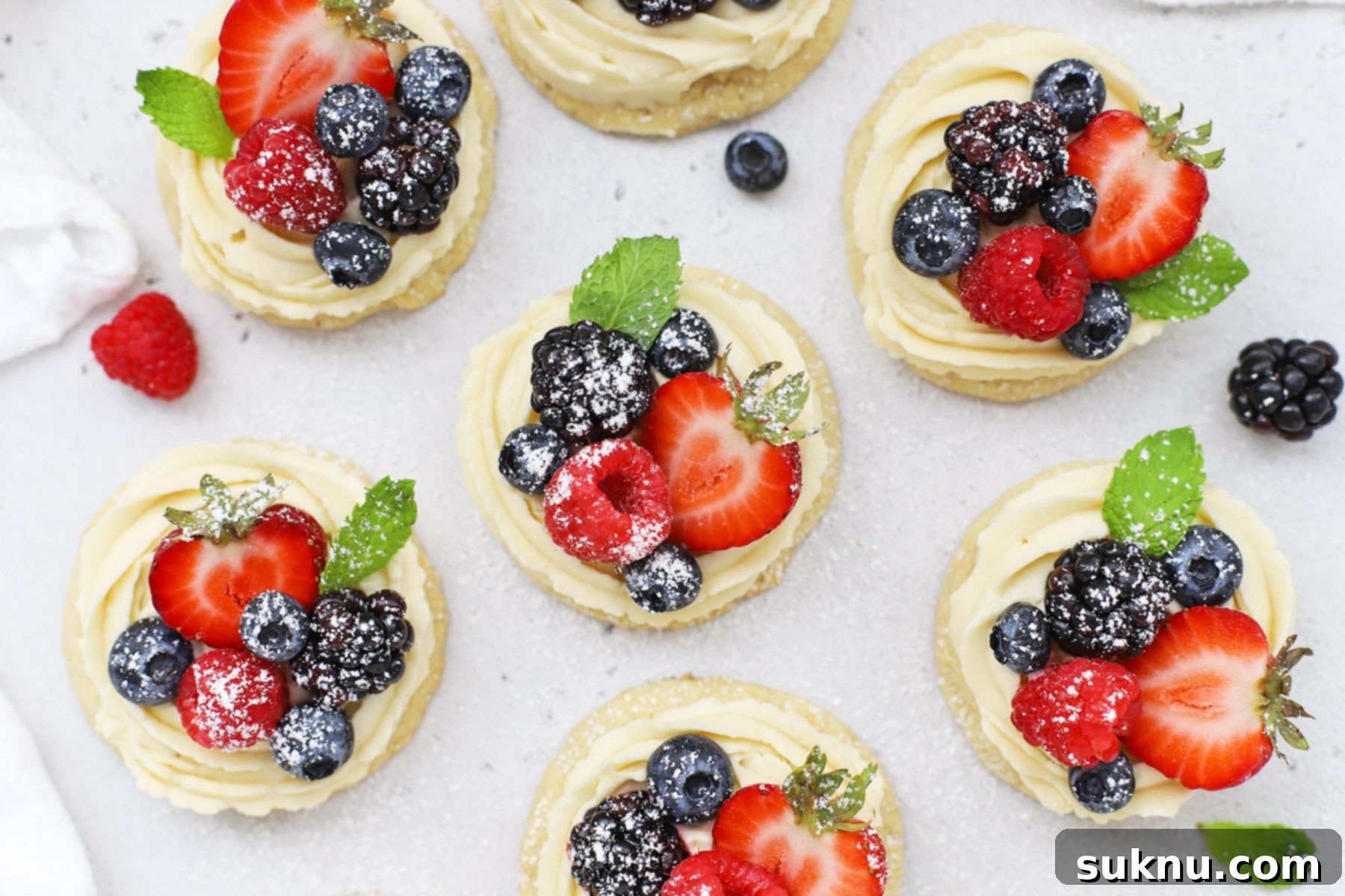 Overhead view of gluten-free fruit pizza cookies topped with cream cheese frosting berries and powdered sugar