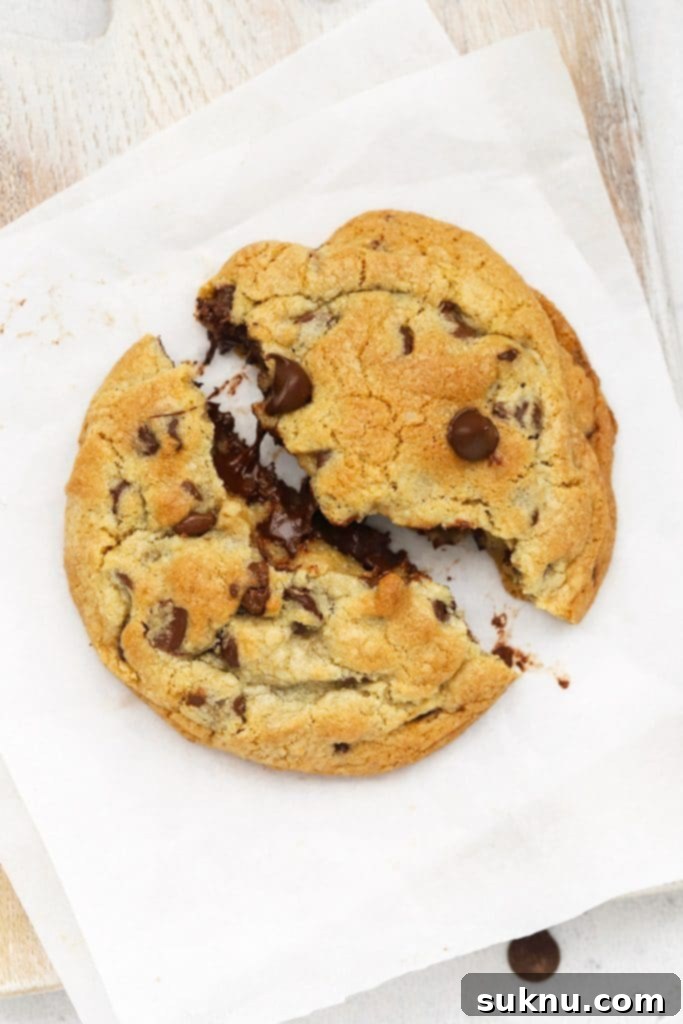 Breaking a gluten-free Levain chocolate chip cookie in half, revealing its gooey center