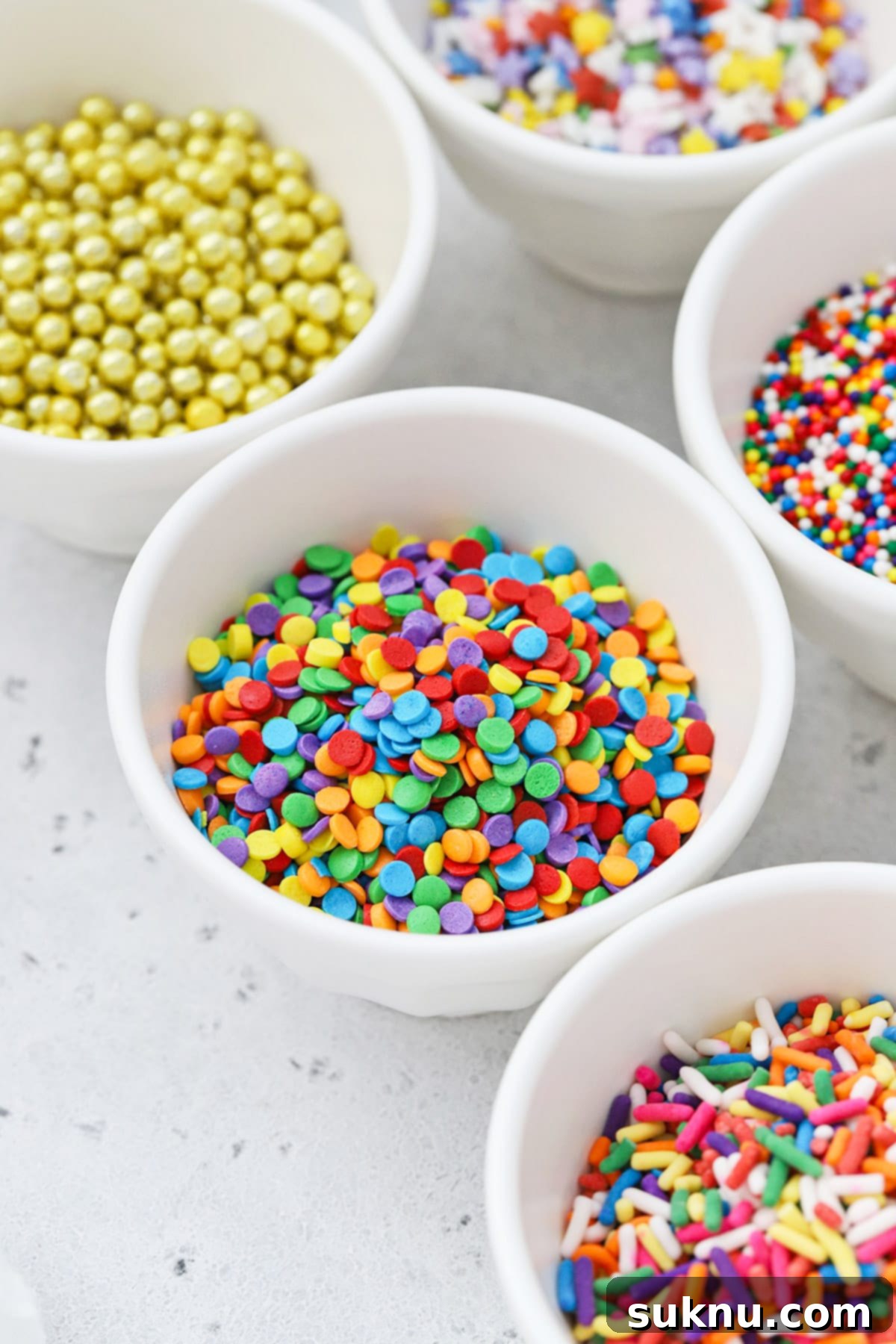 Different kinds of colorful sprinkles in white bowls