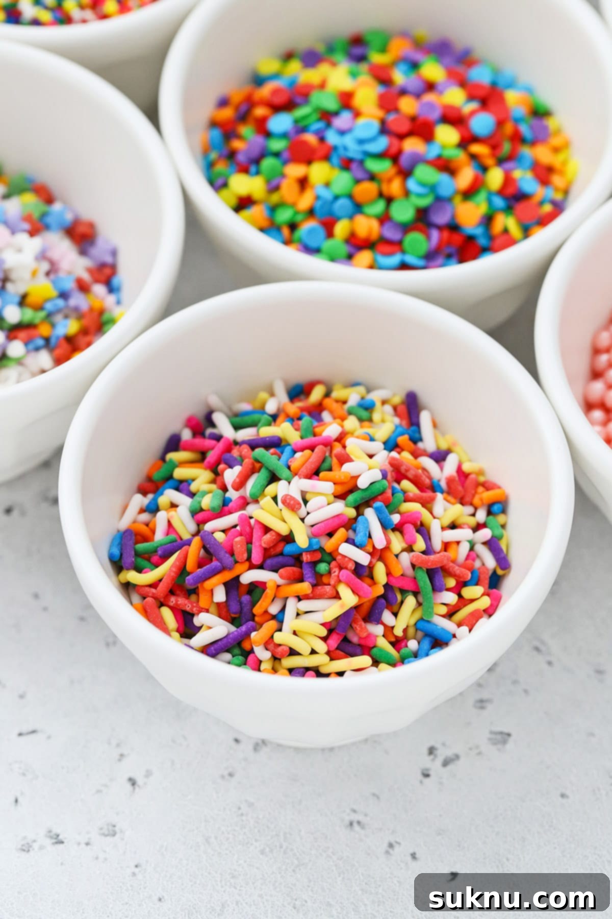 Different kinds of colorful sprinkles in white bowls