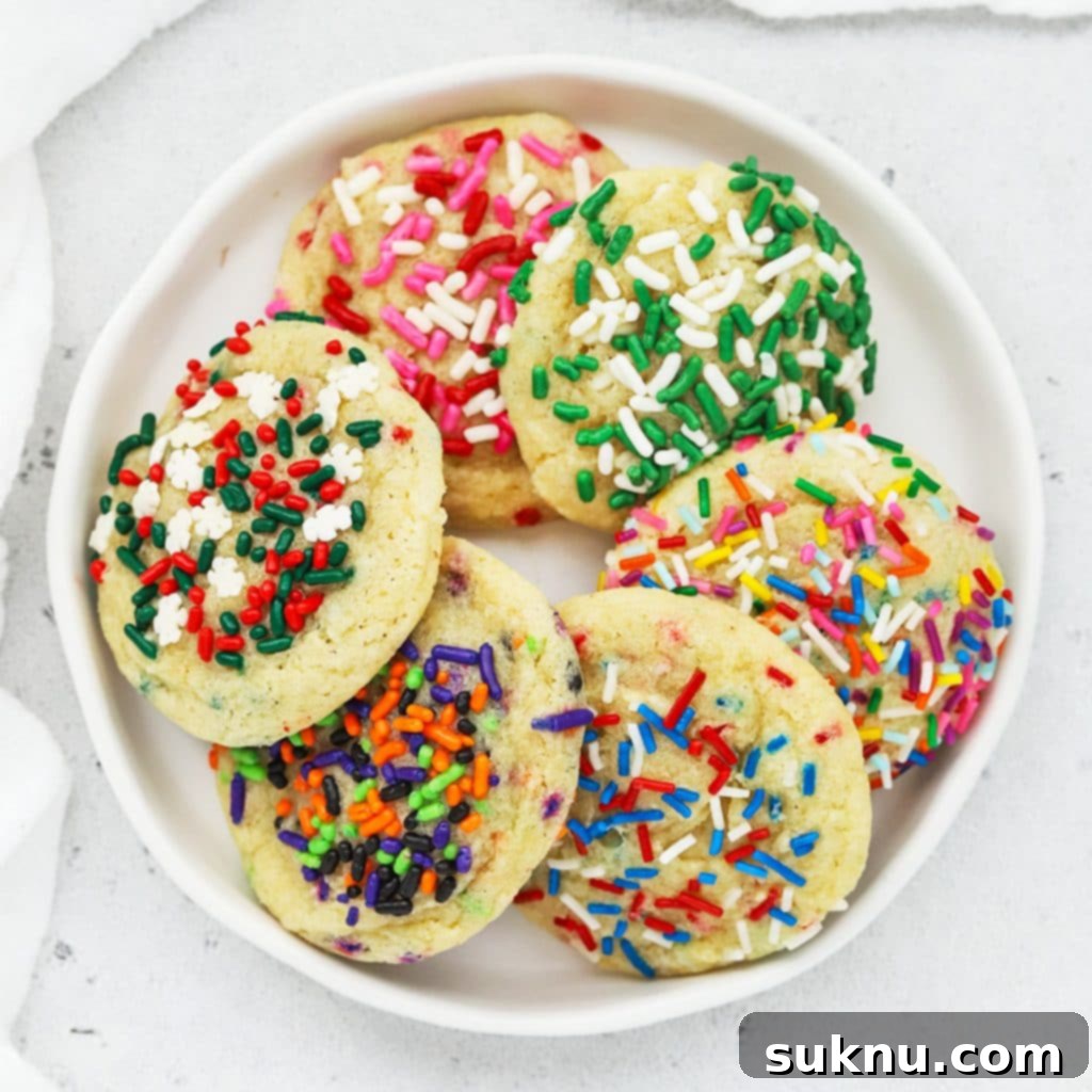 Overhead view of six gluten-free sprinkle sugar cookies with different colored sprinkles for each holiday--pink, red and white for valentine's day, white and green for st. patrick's day, pastels for Easter, red white and blue for 4th of July, green, black, orange, and purple for halloween, and red, white and green for christmas.