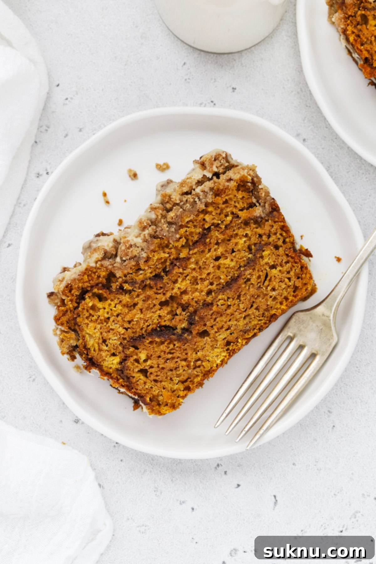 Overhead view of beautifully sliced gluten-free cinnamon swirl pumpkin bread, topped with a golden streusel and glistening maple glaze, presented on a rustic wooden board