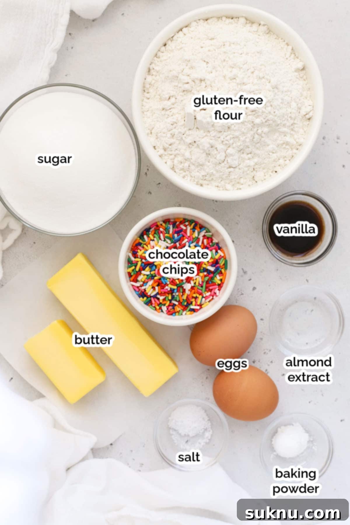 Sprinkled Gluten Free Sugar Cookies 3 A collection of ingredients neatly laid out on a counter, ready for making gluten-free sprinkle sugar cookies, including butter, sugar, eggs, flour, and a variety of colorful sprinkles.