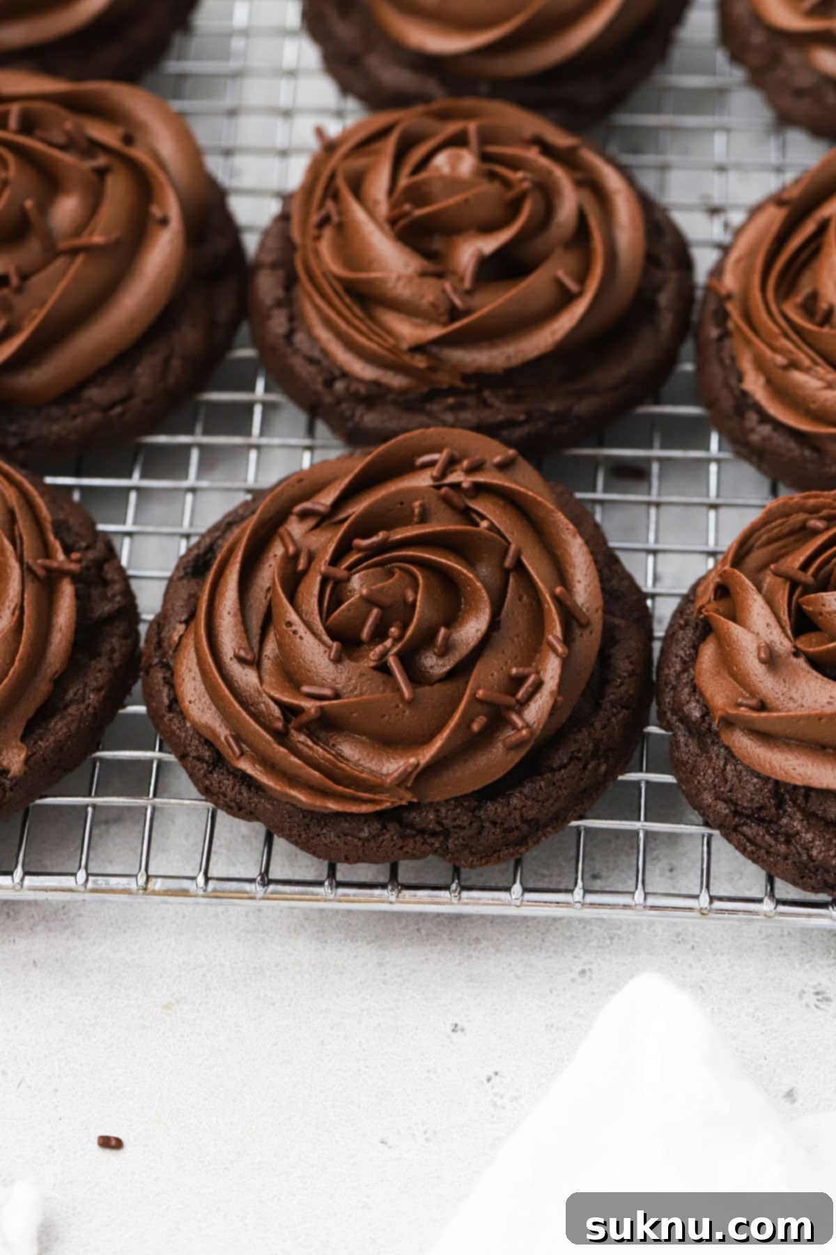 Gluten-free Crumbl chocolate cake cookies with chocolate frosting on a wire rack, ready to be served.