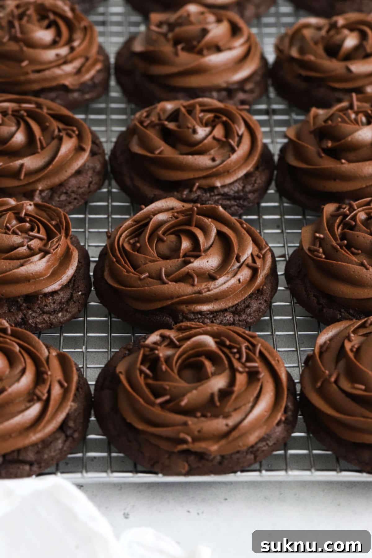 Gluten-free Crumbl chocolate cake cookies with chocolate frosting on a wire rack, highlighting their perfect rosettes.