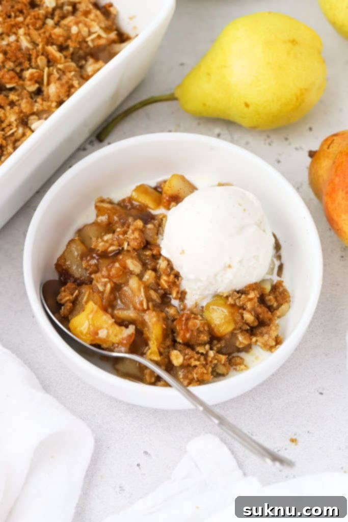 Spoon digging into a bowl of gluten-free pear crisp topped with melting vanilla ice cream and caramel sauce.