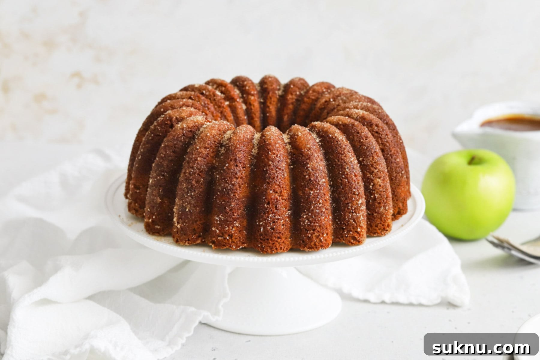 Gluten-Free Apple Spice Bundt Cake on a white cake stand, dusted with cinnamon sugar.