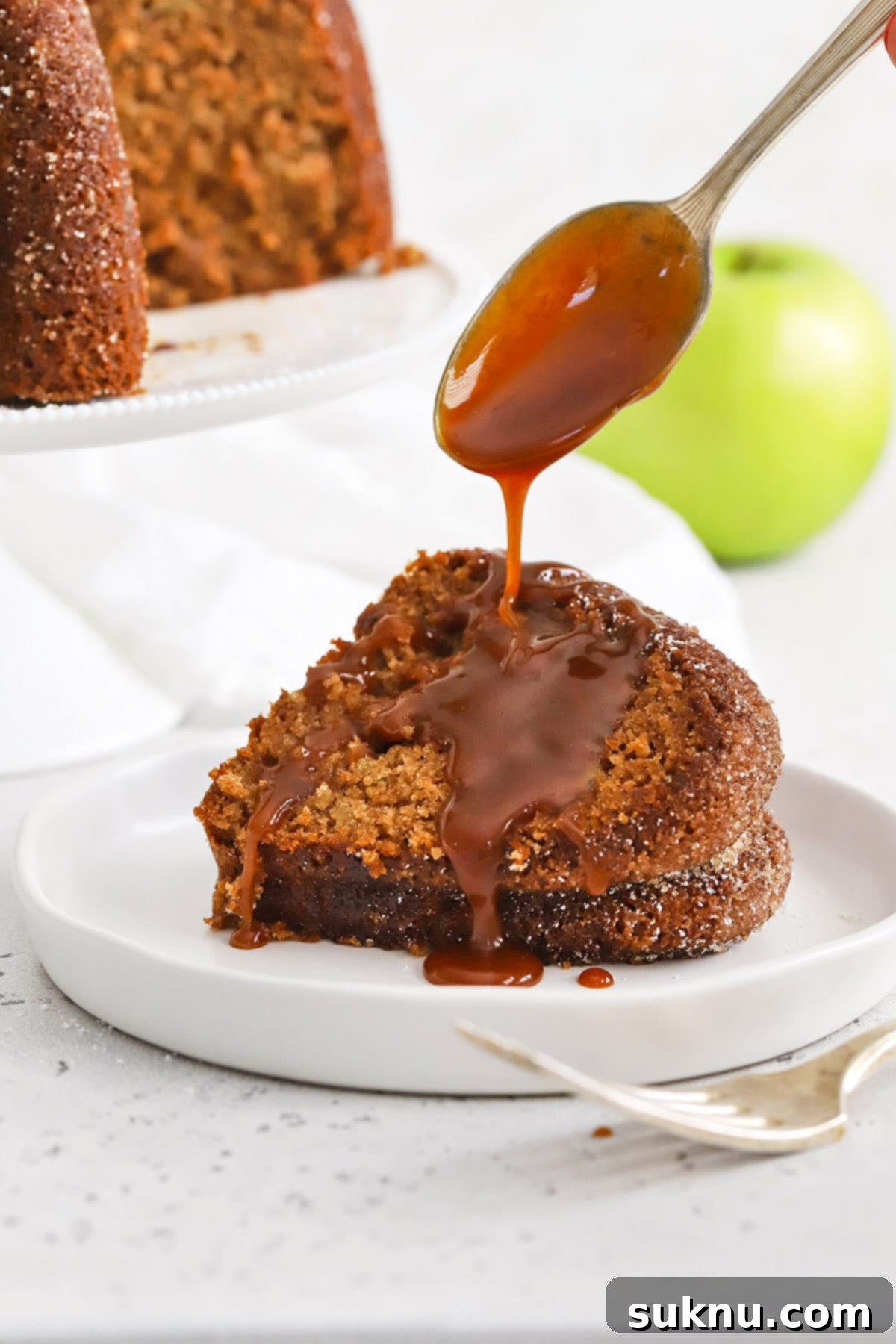 A slice of gluten-free apple spice bundt cake being artfully drizzled with warm caramel sauce, ready to serve.