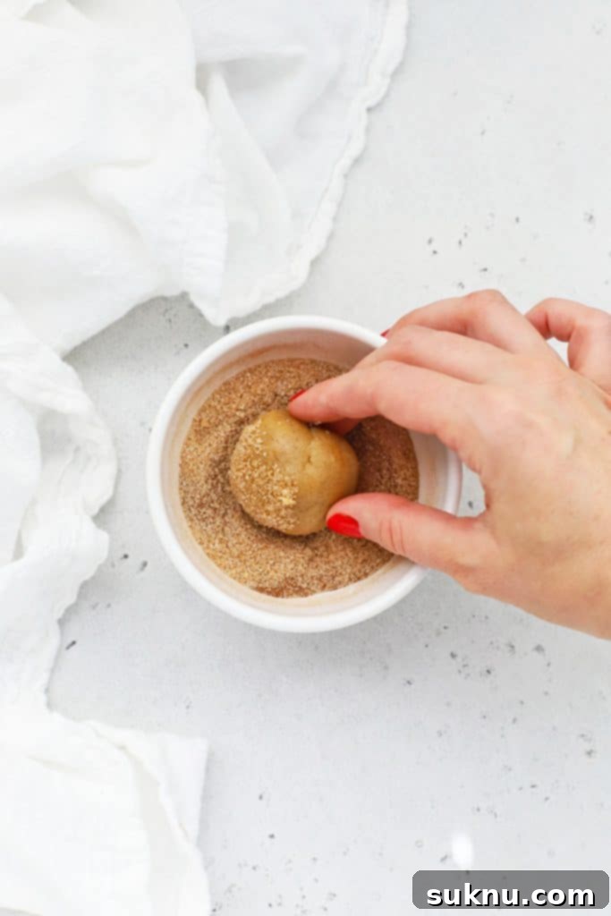 Rolling balls of gluten-free snickerdoodle cookie dough in cinnamon sugar