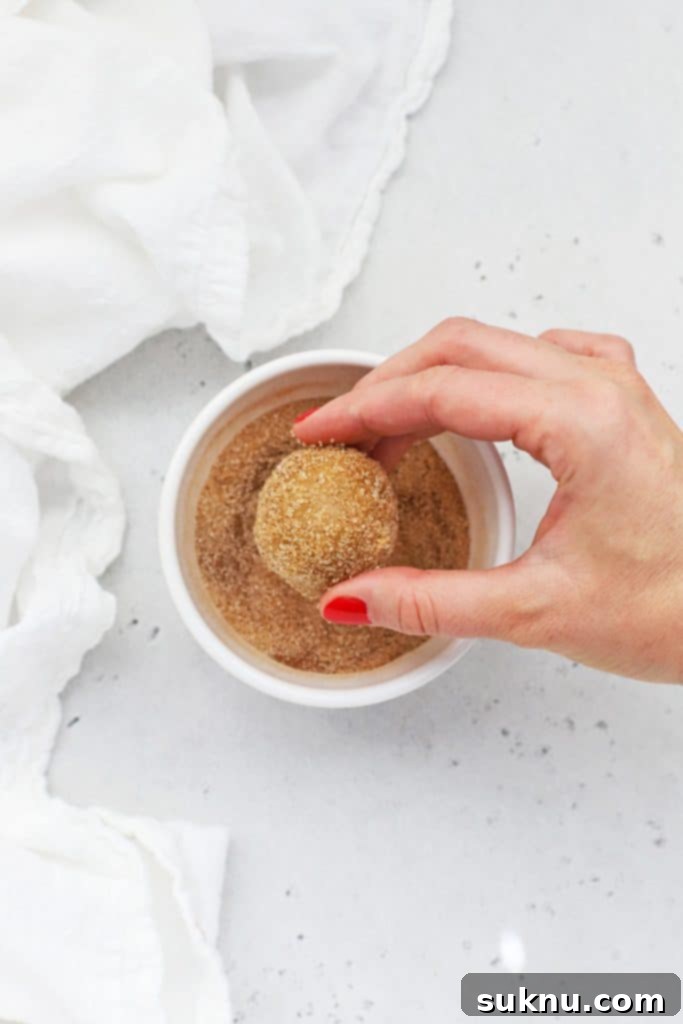 Rolling balls of gluten-free snickerdoodle cookie dough in cinnamon sugar