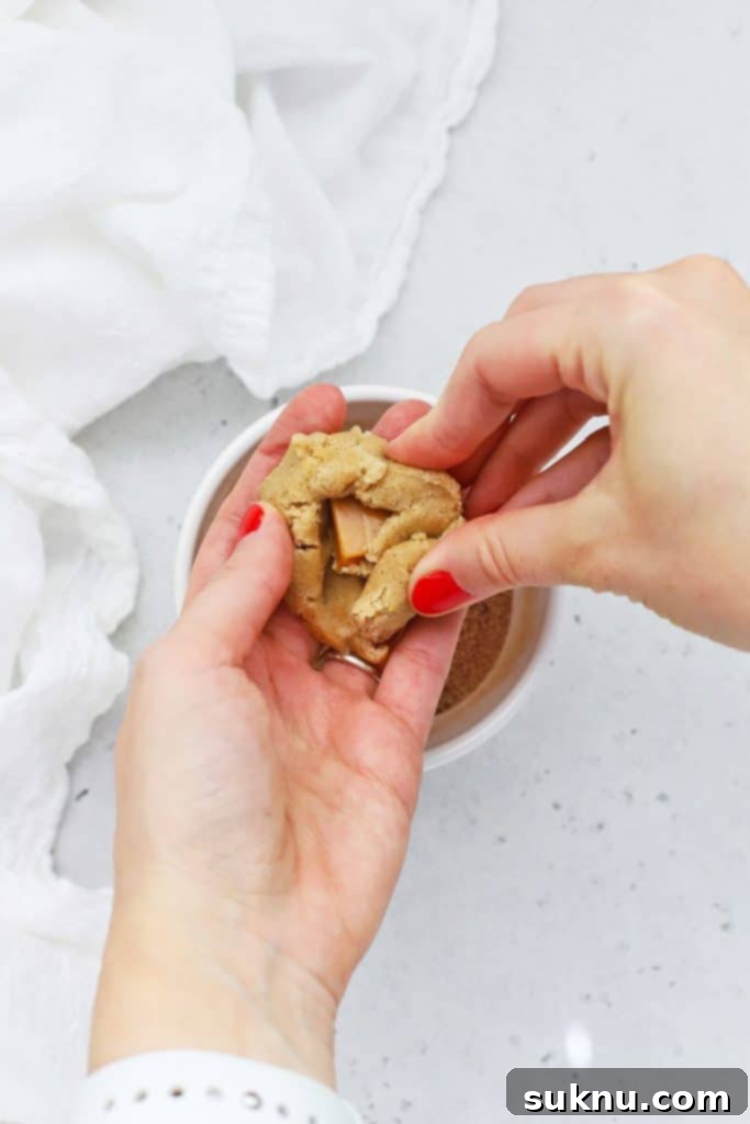 Folding gluten-free snickerdoodle cookie dough around half of a caramel