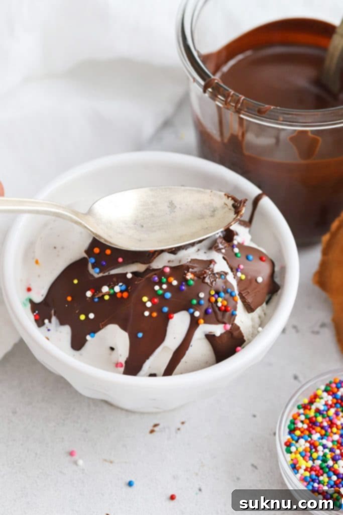 Transform Your Ice Cream: 2-Ingredient Magic Chocolate Shell 7 Cracking the homemade magic chocolate shell on a scoop of vanilla ice cream with a spoon, revealing the crunchy texture