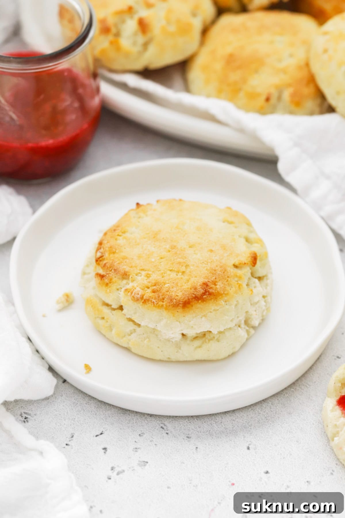 A plate of golden-brown, fluffy gluten-free biscuits, with a side of vibrant raspberry freezer jam.