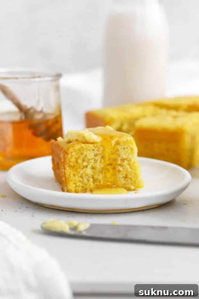 A slice of fluffy gluten-free cornbread generously topped with melted honey butter, presented on a plate.