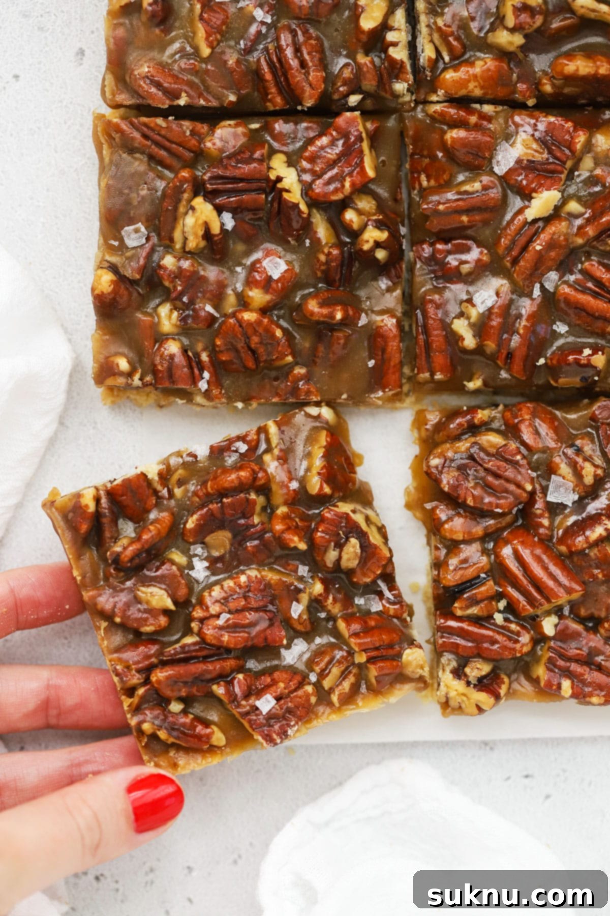Sweet and Salty Gluten-Free Pecan Caramel Treats 7 Hand picking up a gluten-free salted caramel pecan pie bar from the tray