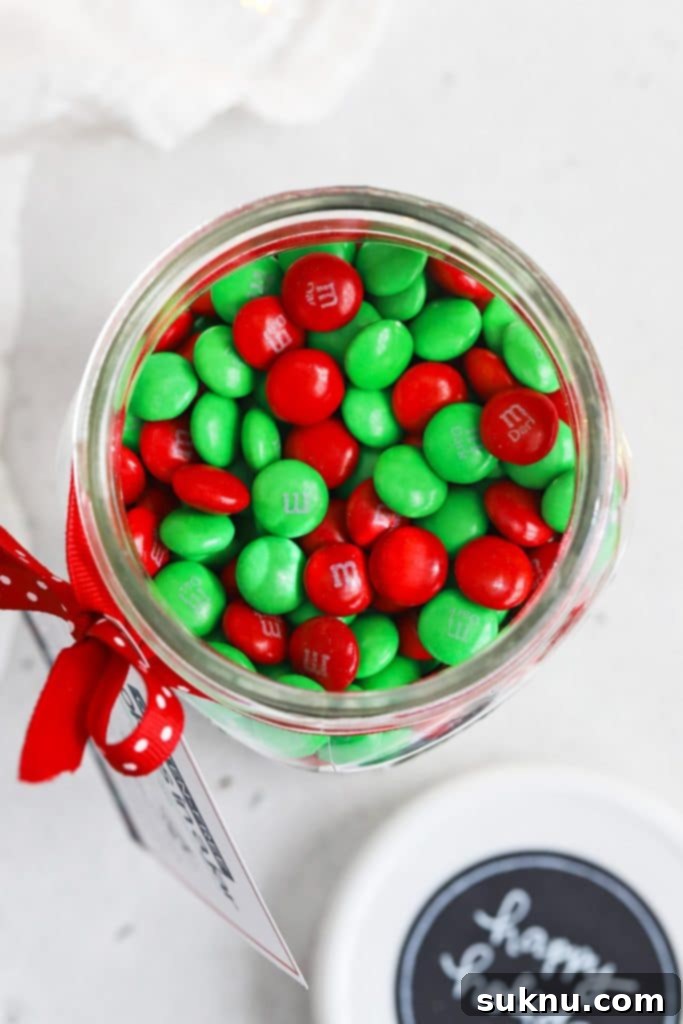 Close-up overhead view of the top layer of festive red and green M&Ms in a gluten-free cookie mix jar, ready for gifting.